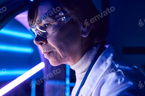 Preview: innovative solutions, portrait of middle aged woman scientist in goggles in neon-lit science center