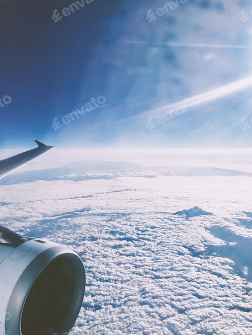 Preview: the wing of an airplane flying above clouds in the sun
