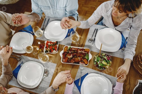 Preview: Above view of multi-generation family saying grace at dining table.