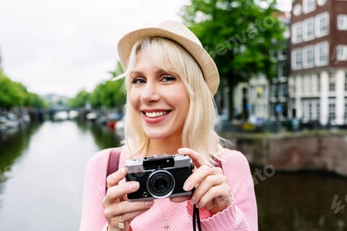 Preview: Portrait of happy young woman holding photo camera over Amsterdam canal.