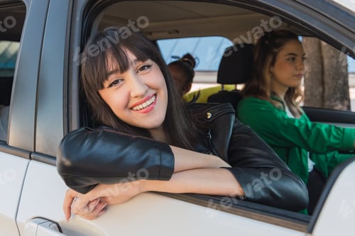 Preview: Cheerful ethnic woman sitting in parked white car near tree trunk