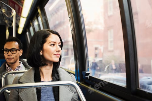 Preview: A young woman sitting on a train looking out of the window at an urban landscape, with a man sitting