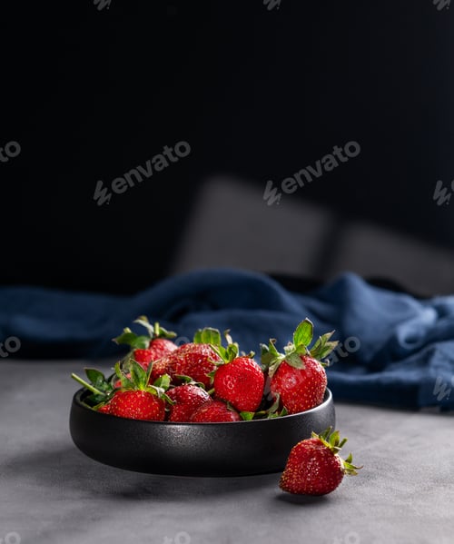 Preview: Strawberries in a black bowl on a dark background with a napkin and shadows.