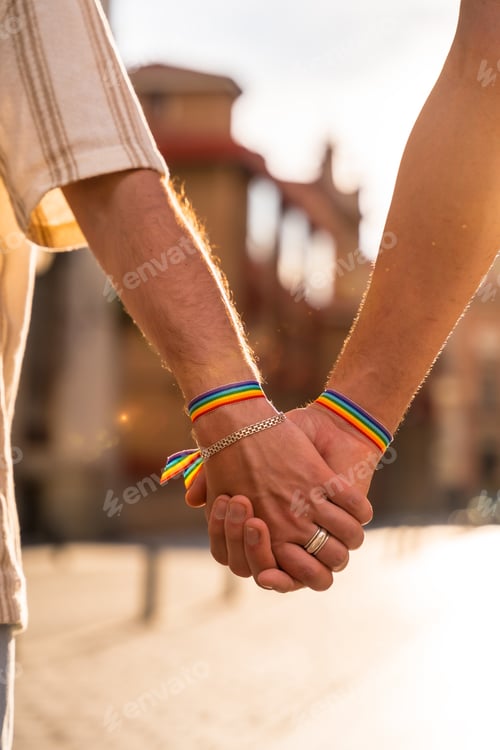 Preview: Detail of the holding hands of a couple of homosexual men with the rainbow flag at the pride party