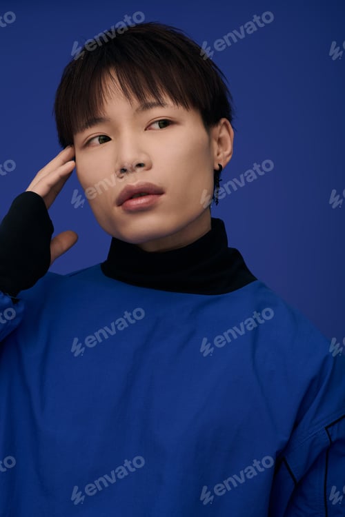 Preview: Young handsome asian man posing with style against a vibrant blue backdrop in a modern setting