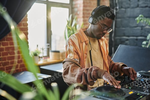 Preview: Young man touching tourntable and turning mixer of dj set while creating music