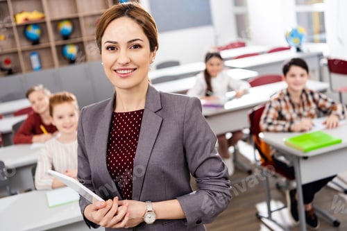 Preview: Smiling teacher with digital tablet standing in front of pupils and looking at camera
