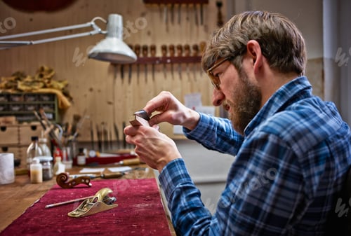 Preview: Violin maker in his workshop examining neck of an instrument
