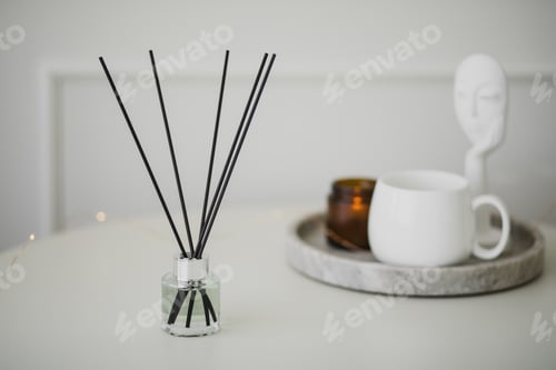 Preview: Still life with white mug, aromatic sticks and candles on a table in a cozy living room.