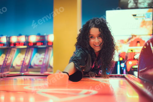 Preview: Excited young woman enjoying an air hockey game at a vibrant arcade