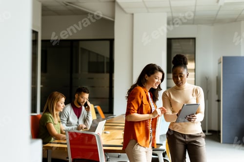 Preview: Two young business women with digital tablet in the office in front of their team