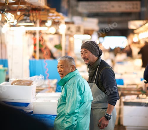 Preview: Two men sharing a cheerful moment at a busy market stall.
