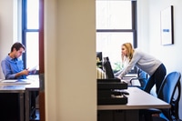 Preview: A shot of a young man sitting in an office looking at a cellphone, and a young woman standing in