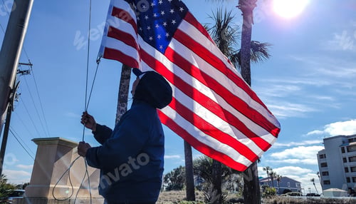 Preview: Young man from behind installing new flag where he manages a beach condo.