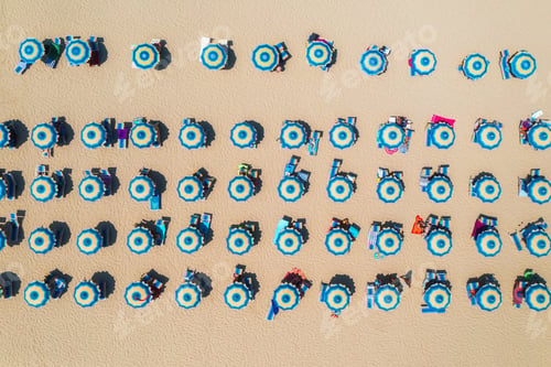 Preview: Aerial view of colorful blue umbrellas on sandy beach at sunset