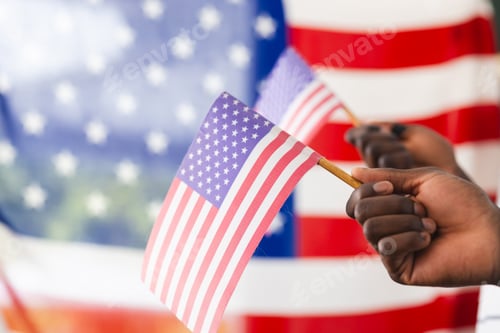 Preview: African American hand holding a small American flag, with a larger flag in the background