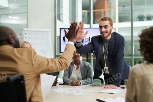 Preview: Young smiling businessman giving high five to African American colleague