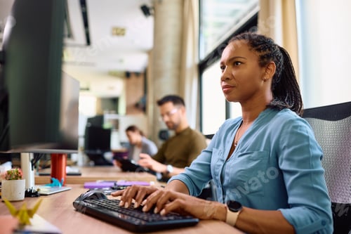 Preview: Black female entrepreneur working on desktop PC in the office.
