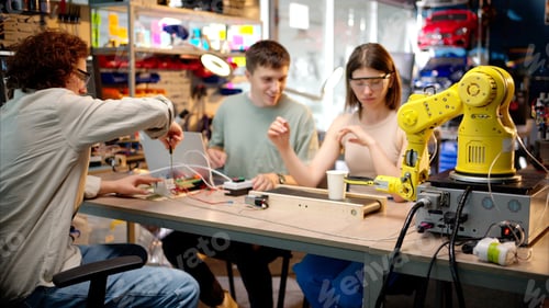 Aperçu: Three young happy engineers fixing an yellow robotic arm in the workshop, computer programming