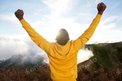 Preview: back of black man in hoodie with hands raised in air and sun in background