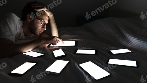 Preview: man using tablet at night chatting in social media, lying in bed around the set of switched-on phone