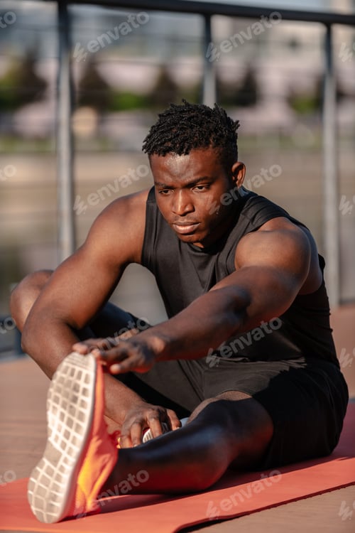 Preview: Confident young African man in sportswear doing stretching exercises outdoors