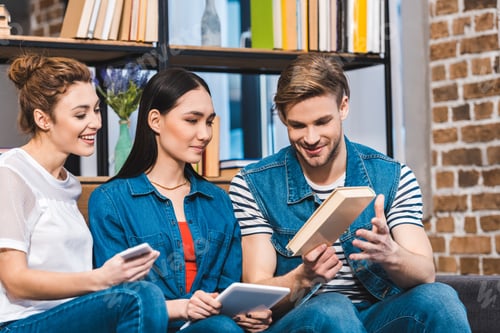 Preview: smiling young man showing book to girls using digital devices