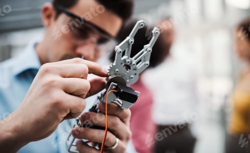A young businessman or scientist with robotic hand standing in office, working.