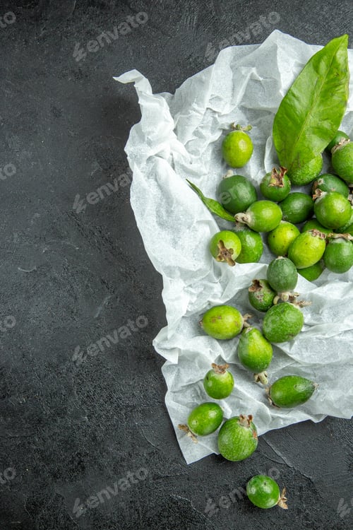 Preview: Vertical view of natural fresh green feijoas with leafs on white page on dark background