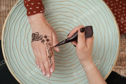 Preview: Professional mehndi master making henna tattoo at table, top view