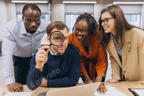 Preview: Interracial business team analyzing data on laptop with magnifying glass, working together
