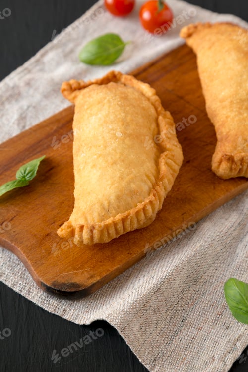 Preview: Homemade Deep Fried Italian Panzerotti Calzone on a rustic wooden board on a black background
