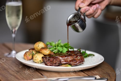 Preview: Person pouring sauce on meat with fried potatoes