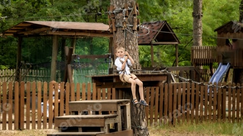 Preview: Portrait of happy cheerful boy riding on the zip line at extreme adventure park. Kids sports