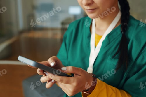 Preview: Asian Woman Wearing Green Scrubs Sitting and Using Tablet