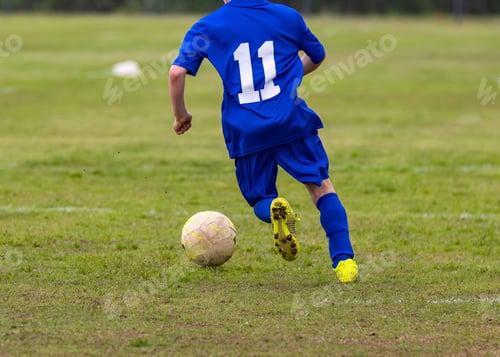 Preview: Young boy wearing a blue jersey is kicking a soccer ball on a soccer field