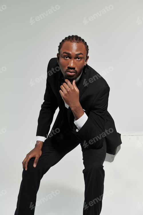 Preview: Young Black man in a classy suit confidently poses against a grey backdrop