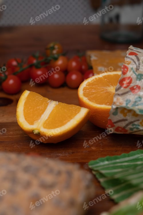 Preview: Sliced orange and tomatoes pouring out of beeswax wrap on a rustic table