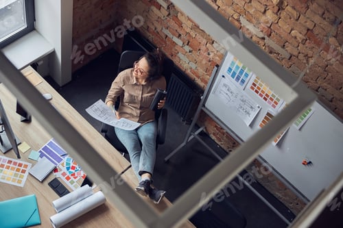 Preview: High angle view of female interior designer looking aside, drinking coffee or tea, holding a