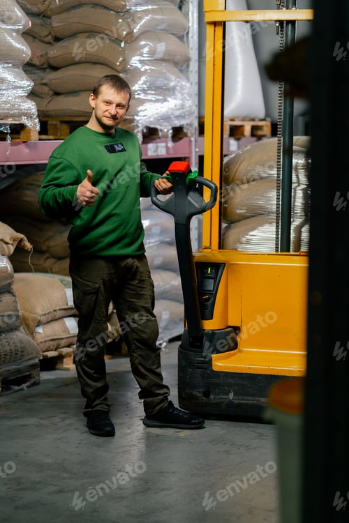 Preview: worker posing at a coffee factory a man with a yellow forklift behind him is carrying bags of coffee