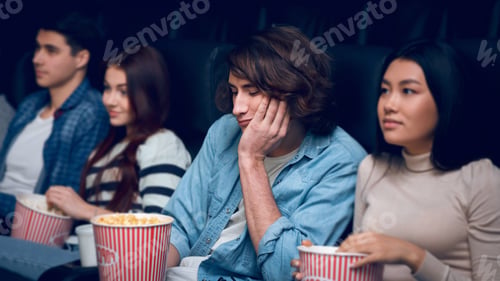 Preview: Handsome young man feeling bored while watching film in cinema