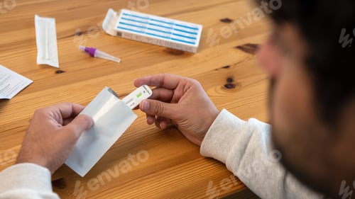 Preview: Caucasian man wearing mask opening a sample of covid-19 antigen test at home.