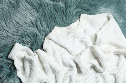 Preview: White knitted sweater on green fur rug, flat lay
