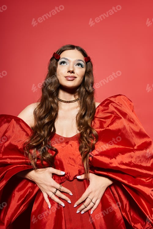 Preview: Young woman in vibrant red gown with dramatic sleeves, posing against a bold red backdrop