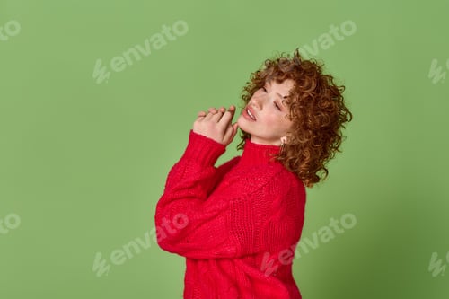 Preview: Young woman with red curls in a cozy sweater poses against a green backdrop