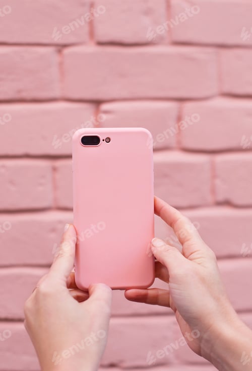 Preview: Woman holding pink mobile phone on a pink brick wall background