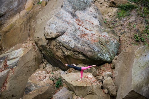 Preview: Sporty fit woman is practicing yoga on the boulder in the nature