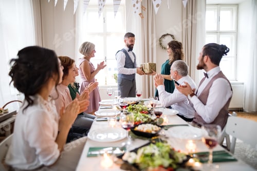 Preview: A man giving gift to a young surprised woman on a family birthday party.