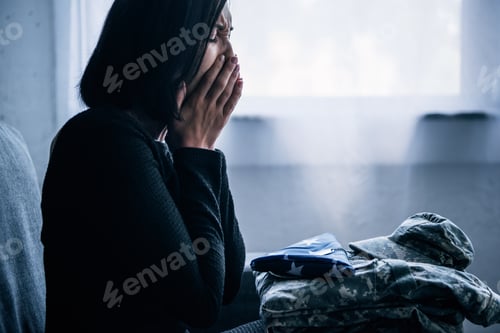 Preview: woman with military clothing and foded american flag crying at home