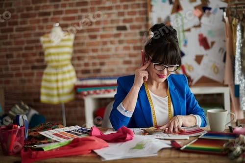 Preview: Woman in design studio sitting at desk, hand on head looking down